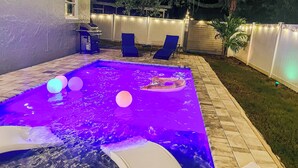 A swimming pool with a built-in slide, surrounded by a deck with lounge chairs and string lights.