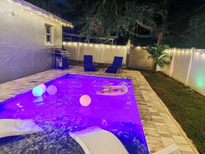 A swimming pool with a built-in slide, surrounded by a deck with lounge chairs and string lights.