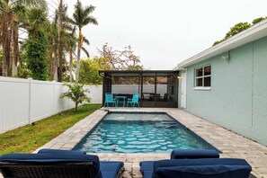 Un patio trasero con piscina, sillas de descanso y un área de porche techado.