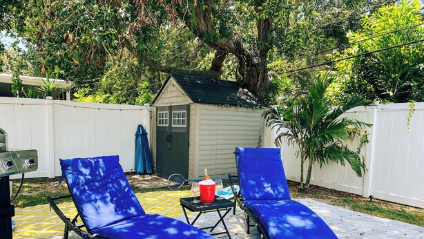 A backyard with two blue lounge chairs, a grill, and a small shed.