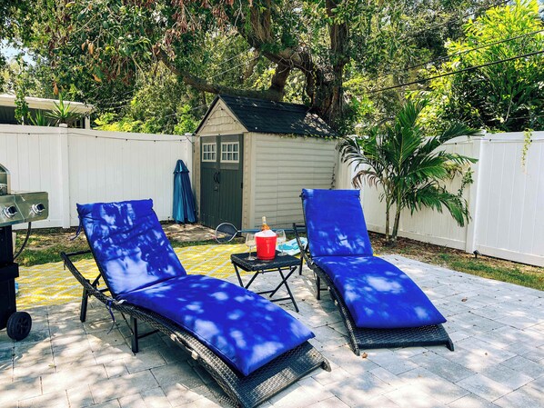 A backyard with two blue lounge chairs, a grill, and a small shed.