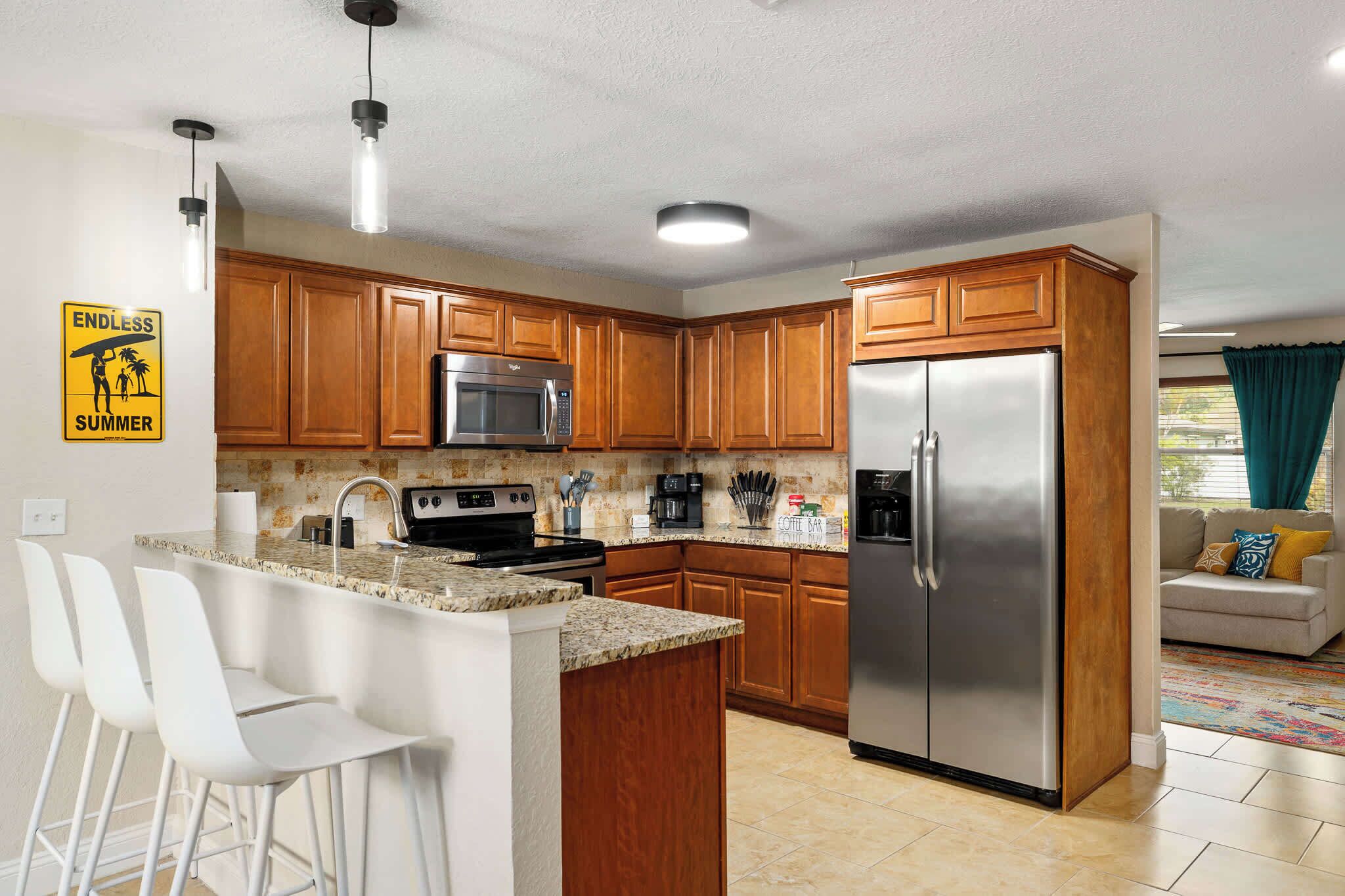 A modern kitchen with wooden cabinets, stainless steel appliances, and a bar area with white stools.