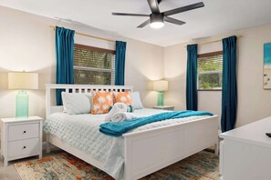 A neatly arranged bedroom with a bed, two bedside tables, a desk, and a ceiling fan.