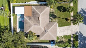 An aerial view of a modern building with a geometric roof design, a swimming pool, and surrounding greenery.