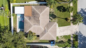 An aerial view of a modern building with a geometric roof design, a swimming pool, and surrounding greenery.