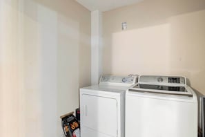 A laundry room with two white front-loading washers and dryers, a small shelf with detergent bottles, and a white wall.