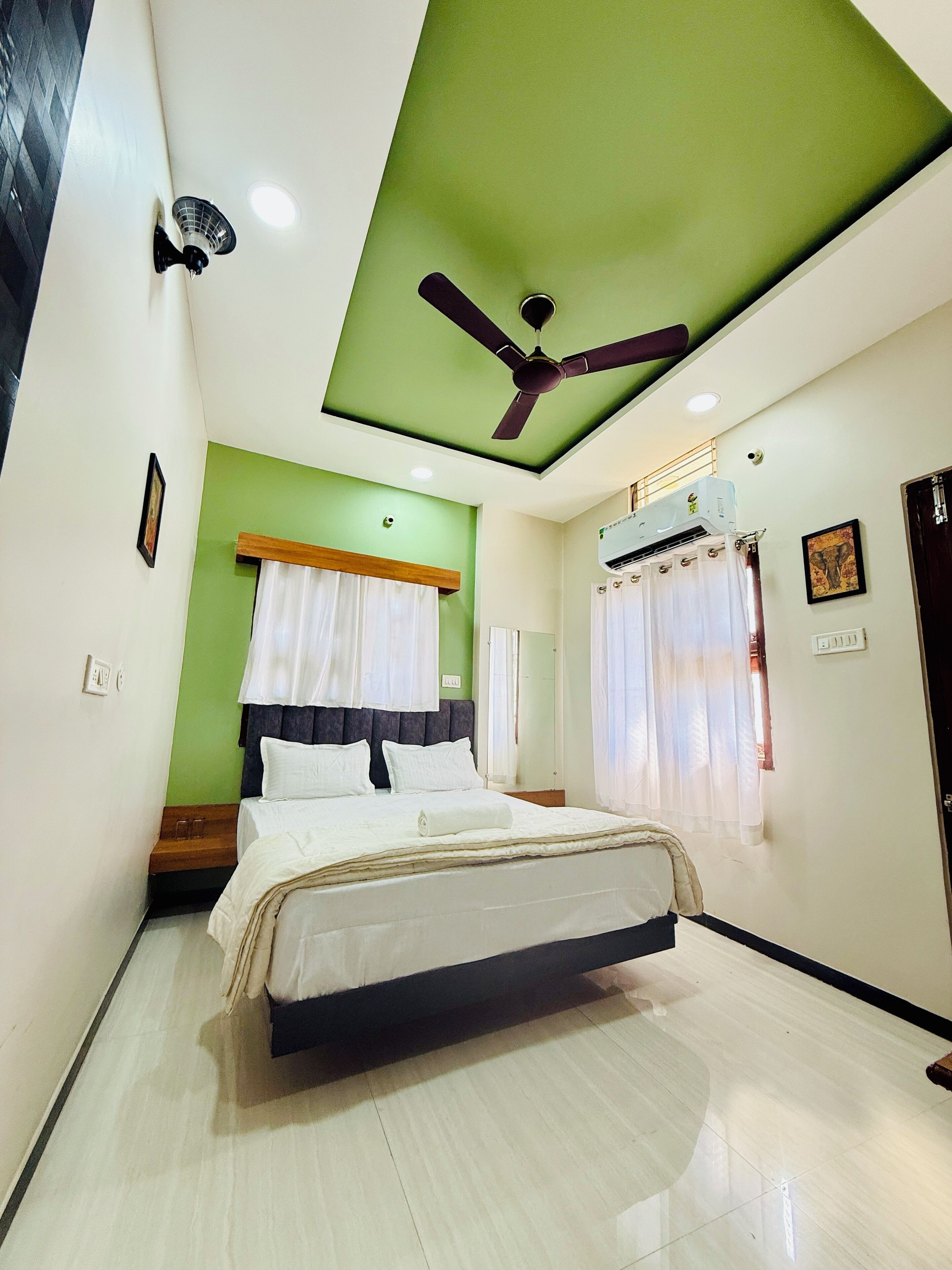 A bedroom with a bed, a ceiling fan, an air conditioning unit, and a window with curtains.