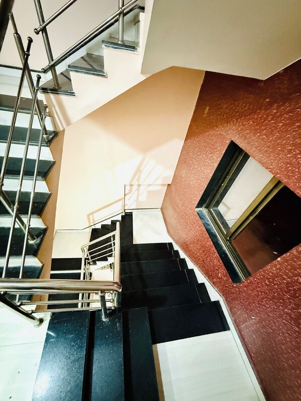 Un interior de varios niveles con una escalera, barandillas metálicas y una combinación de paredes negras y beige.