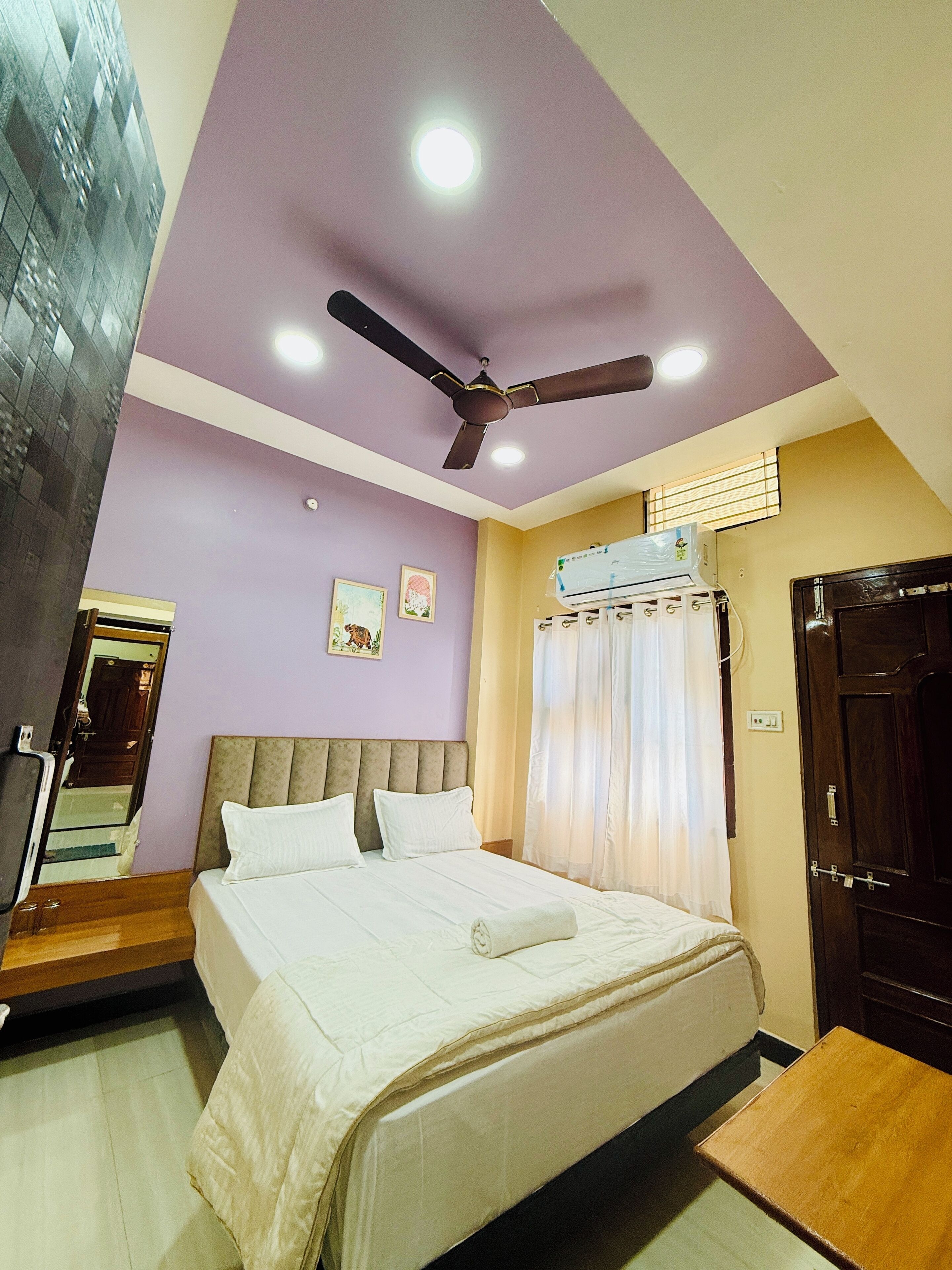 A bedroom with a bed, ceiling fan, air conditioning unit, and a door.