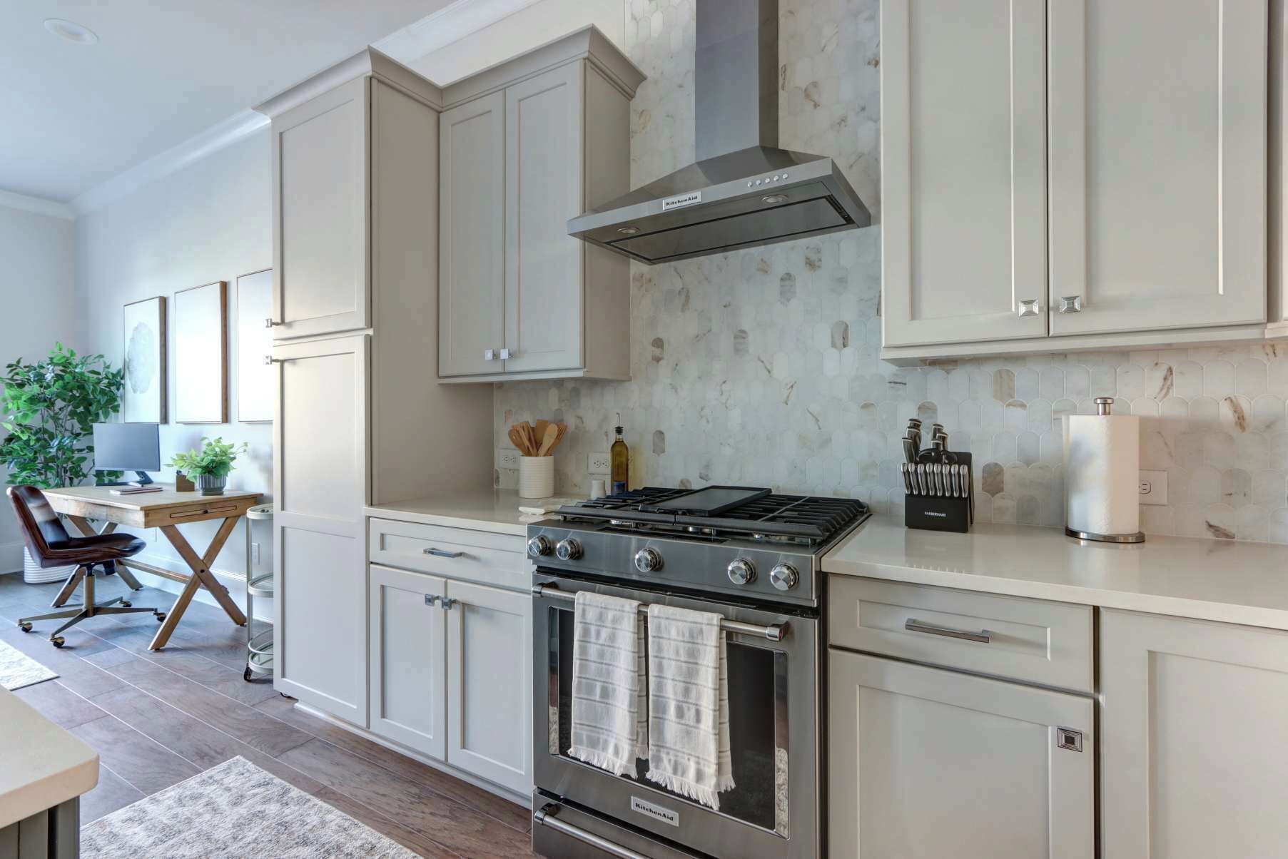 Une cuisine moderne avec des meubles blancs, une cuisinière en acier inoxydable et un pare-feu orné d’un motif géométrique.