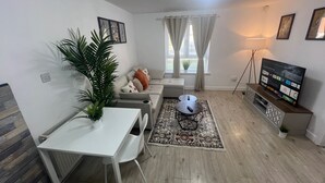 A modern living room with a white sofa, a small round table, a white desk, and a television on a wooden stand.