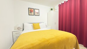A bedroom with a bed, white nightstands, a wardrobe, and red curtains.