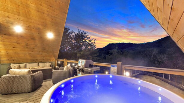 A hot tub with a view of a sunset over a forested hill. - NEW Modern A-Frame w/Hot Tub! (Sevierville)