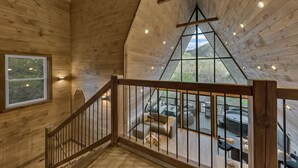 A wooden interior with a high ceiling, a staircase, and a seating area with outdoor views. - NEW Modern A-Frame w/Hot Tub! (Sevierville)