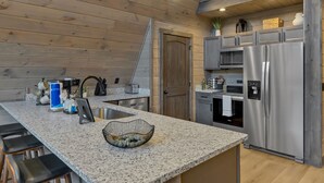 A modern kitchen with granite countertops, stainless steel appliances, and wooden paneling. - NEW Modern A-Frame w/Hot Tub! (Sevierville)