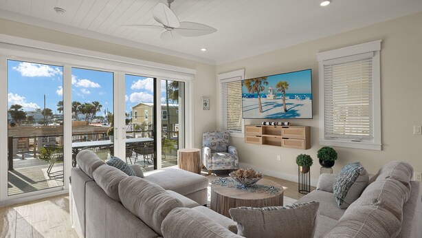 A spacious living room with a large gray sofa, a round coffee table, and a painting of a beach scene. - Villa Capri · 2025 Luxury Build · Steps to Beach (Fort Myers Beach)