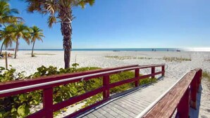 A wooden boardwalk leading to a sandy beach with palm trees and a clear blue sky. - Villa Capri · 2025 Luxury Build · Steps to Beach (Fort Myers Beach)