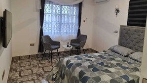 A hotel room with a bed, two chairs, a small table, and a window with curtains. - King George Lodge  (Tema)