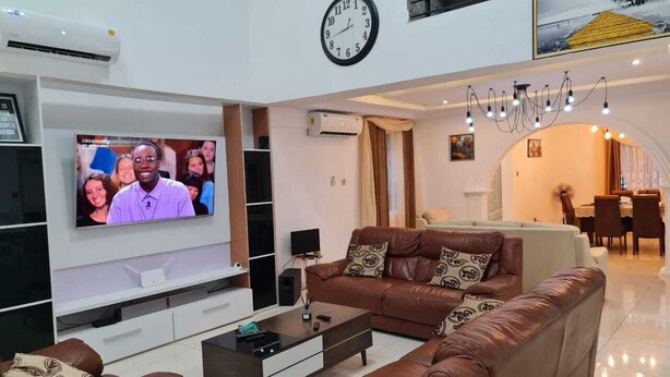 A modern living room with a large flat-screen TV, leather sofas, a coffee table, and a dining area in the background. - King George Lodge  (Tema)