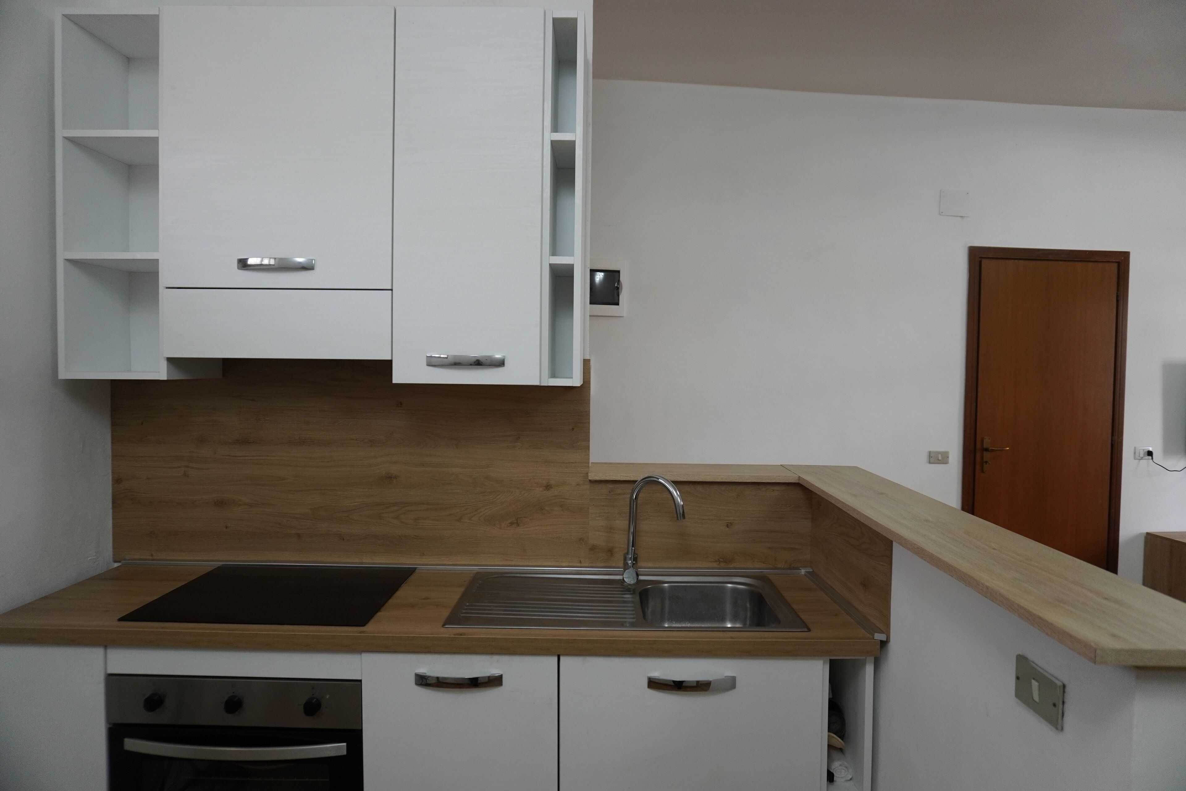 Una cocina moderna con armarios blancos, encimera de madera, pileta de acero inoxidable y horno empotrado.