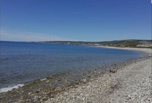 A rocky beach with clear blue water and a distant shoreline.