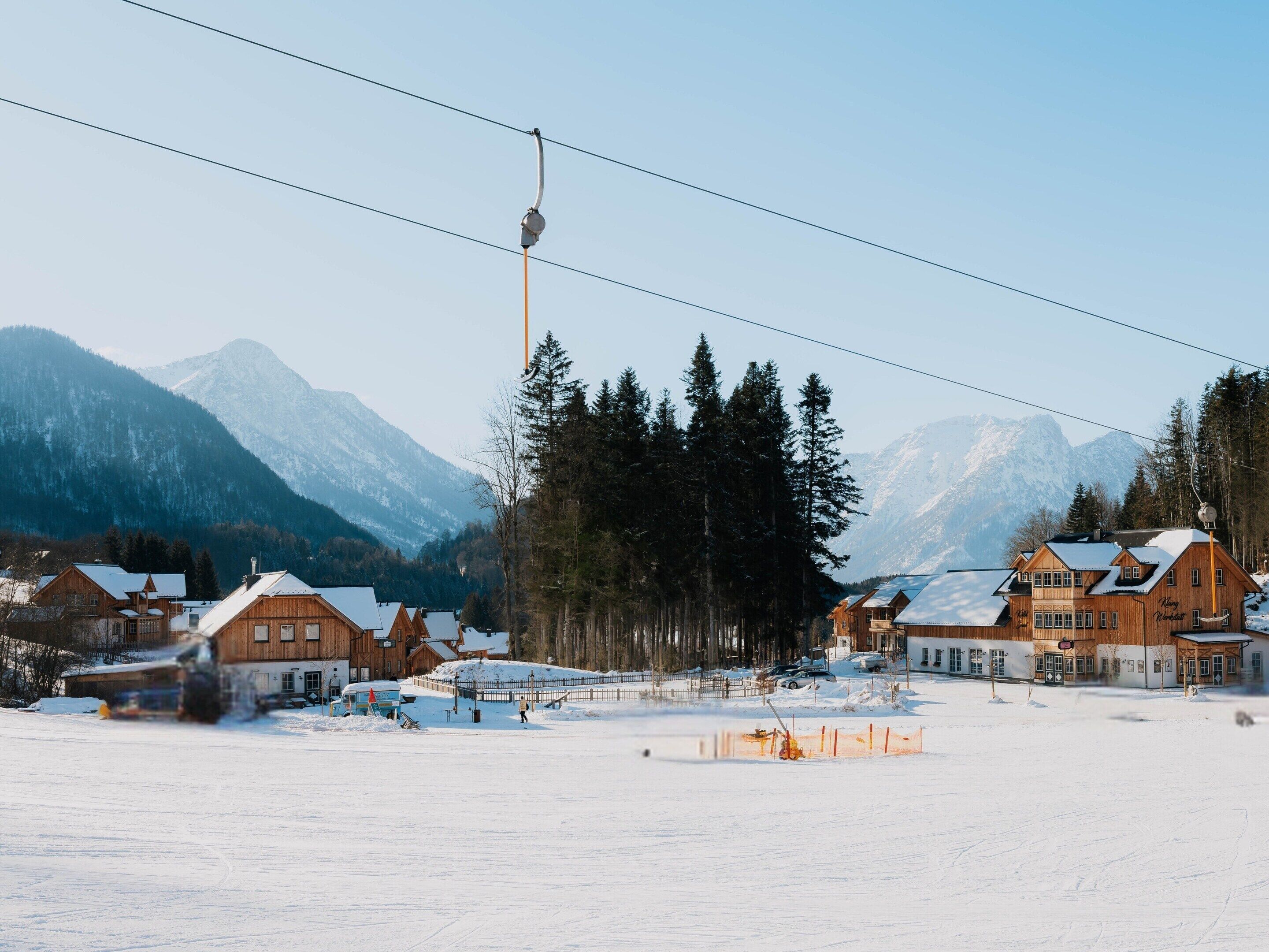 Une station de ski enneigée, avec des chalets en bois, un télésiège et des montagnes en arrière-plan.