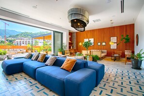 A modern hotel lobby with a large blue sectional sofa, wooden panel walls, and a view of the cityscape.