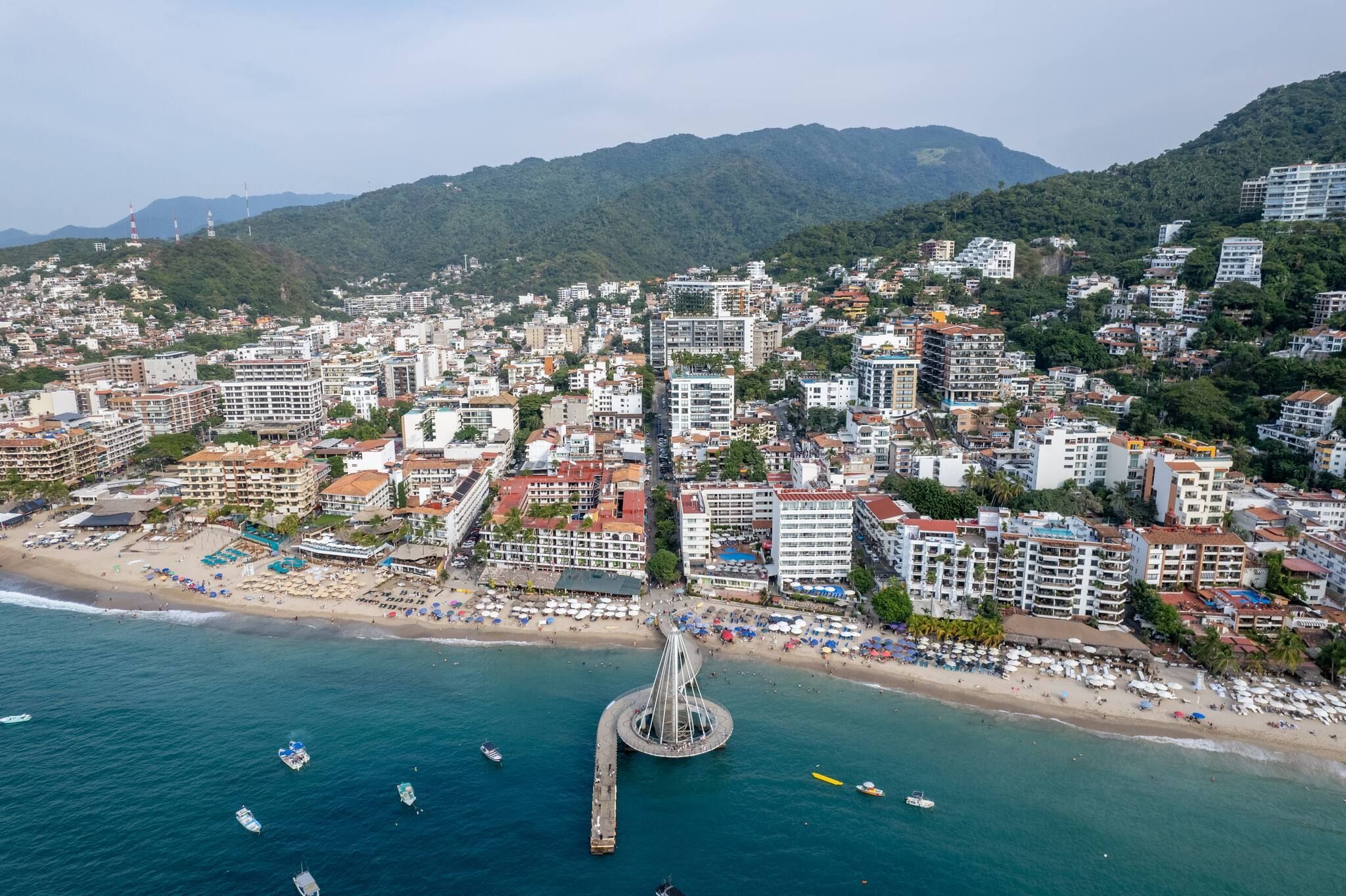 Vista aerea di una città costiera con un molo importante, numerosi edifici e una zona spiaggia.