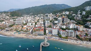 Una veduta costiera di una città con un molo prominente che si protende nel mare, circondata da edifici affollati e una spiaggia con numerosi ombrelloni.