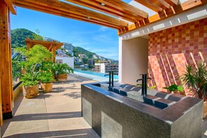 Una terraza en la azotea con piscina, plantas en macetas y vistas a un pueblo en la ladera.