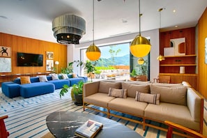 A modern living room with a sofa, a coffee table, and a TV. There are plants and a bookshelf.