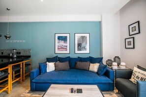 Una sala de estar moderna con un sofá azul, una mesa de centro y una cocina al fondo.