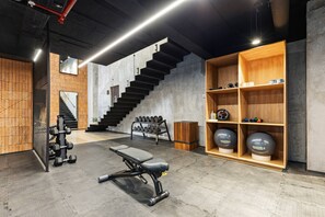 A gym with a staircase, weight bench, dumbbells, and exercise balls.