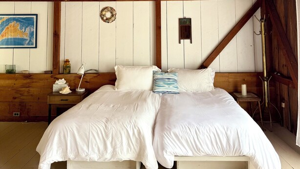 Ein Schlafzimmer mit Holzbalkendecke, einem Bett mit weißer Bettwäsche, einem Nachttisch, einer Karte an der Wand und einem kleinen Tisch mit einer Lampe.