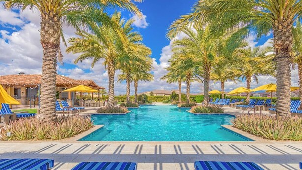 Zona de piscina con palmeras, sillones reclinables azules y sombrillas amarillas.
