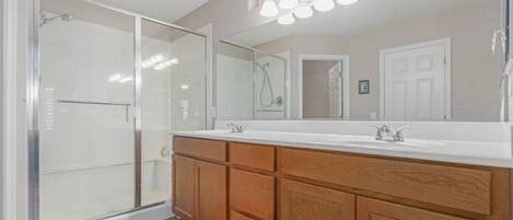 A modern bathroom with a glass shower enclosure, a double vanity with wooden cabinets, and a large mirror.