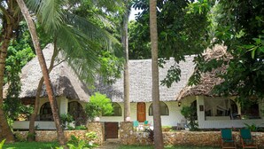 Ein Haus mit Strohdeckung, einer Steinsäule und einem Garten mit Palmen.
