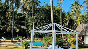 Eine weiße Laube mit einem Bett, umgeben von einem Pool und Palmen.