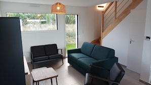 A modern living room with a sofa, chairs, a small table, and a staircase. - Recent house facing the dunes and Grève Blanche beach, at the foot of the GR34. (Plouguerneau)