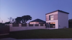 A modern two-story house with a flat roof, a visible garage, and a well-maintained lawn. - Recent house facing the dunes and Grève Blanche beach, at the foot of the GR34. (Plouguerneau)