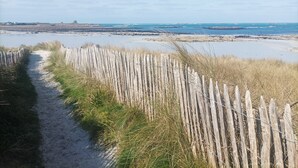 A sandy path leading to a beach with a wooden fence and grass. - Recent house facing the dunes and Grève Blanche beach, at the foot of the GR34. (Plouguerneau)