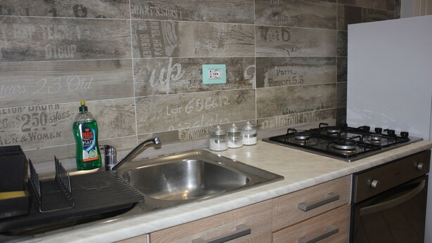 A kitchen with a stainless steel sink, a gas stove, and wooden cabinets. - Tre Cuori - Amy. (Genova)