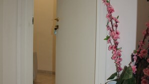 A hallway with a white door, a potted plant with pink flowers, and a bulletin board on the wall. - Tre Cuori - Amy. (Genova)