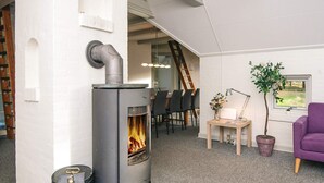 Ein modernes Wohnzimmer mit Kaminofen, Essbereich mit Stühlen, einem violetten Sofa und einem Topf mit Pflanze.