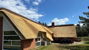 Ein Haus mit einem Strohdach und Backsteinwänden, einem großen Fenster und einem Schornstein.