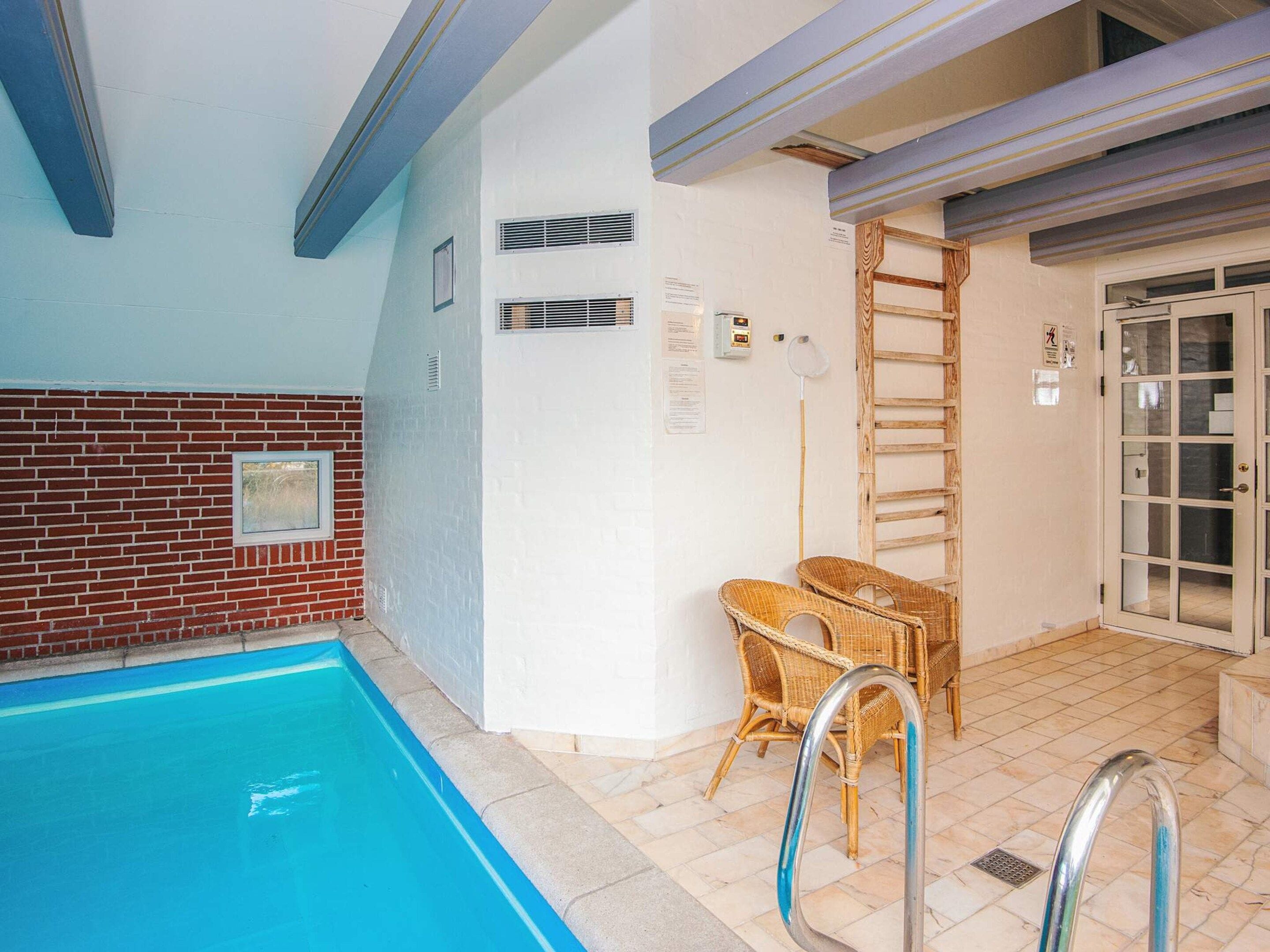 An indoor swimming pool with a tiled floor, a brick wall, and a wooden ladder.