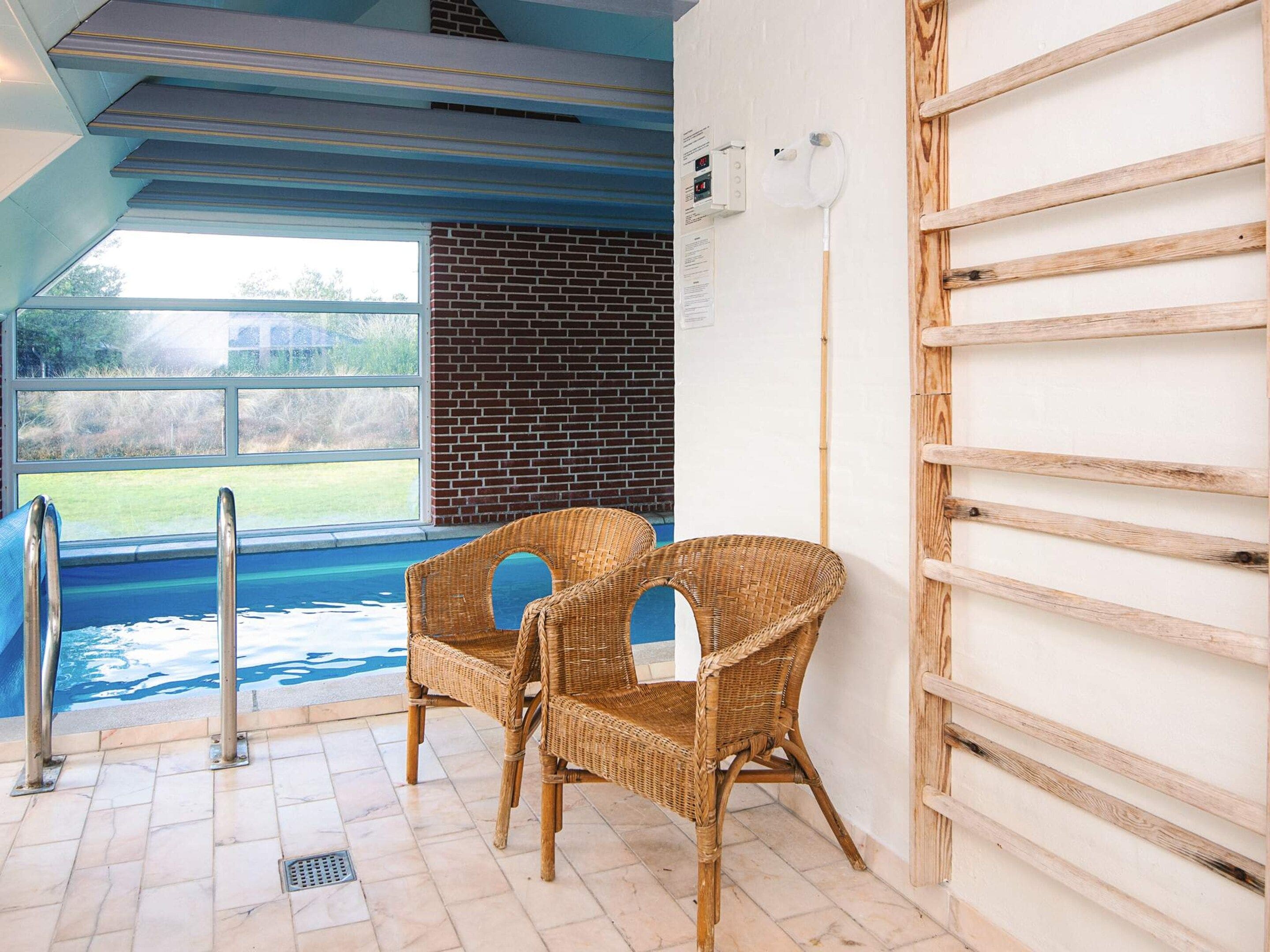 Espaço de spa com hidromassagem, duas cadeiras de vime, uma escada de madeira e vista para o exterior.