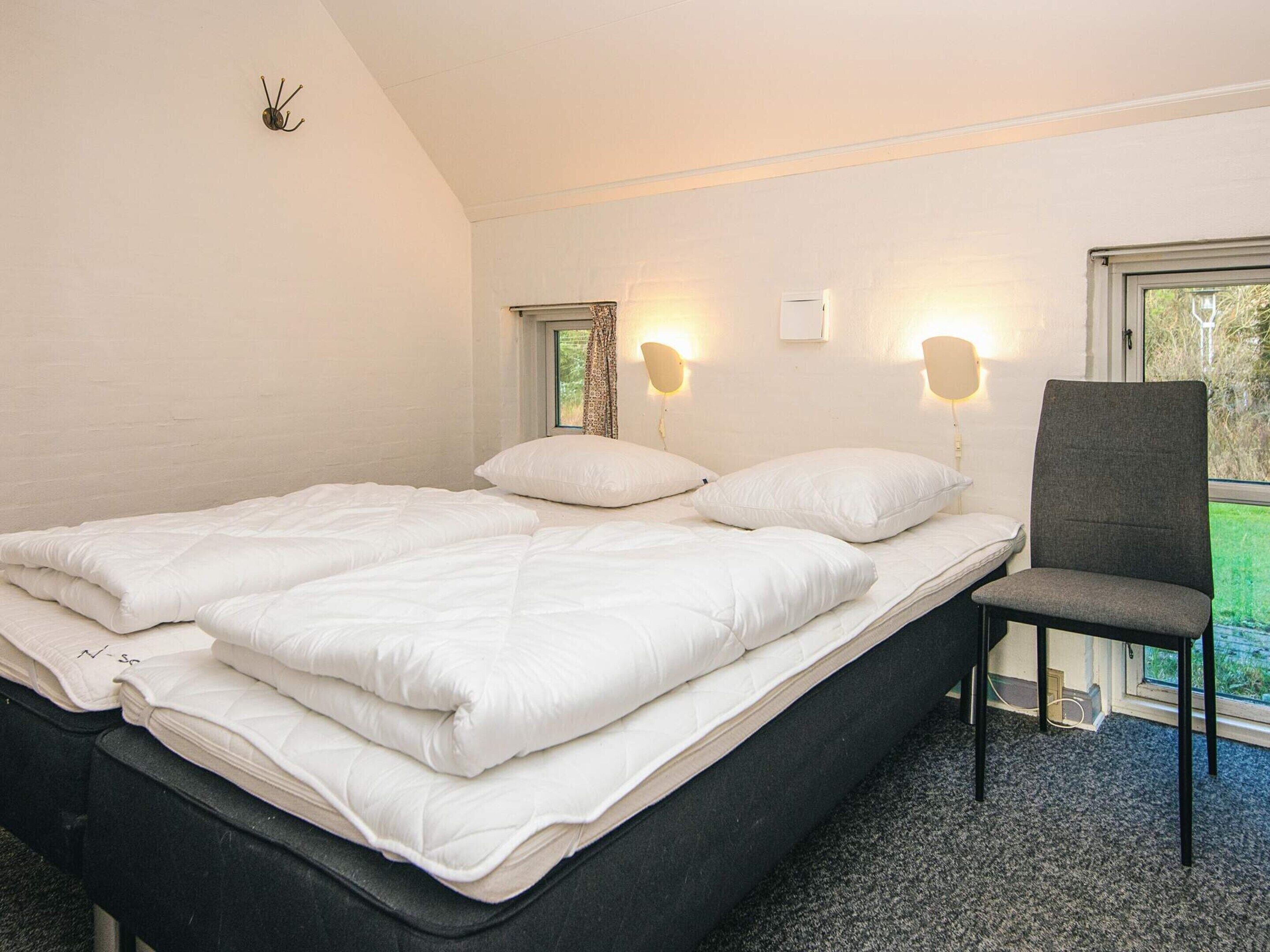 A bedroom with a bed, pillows, a chair, and two wall-mounted lights.