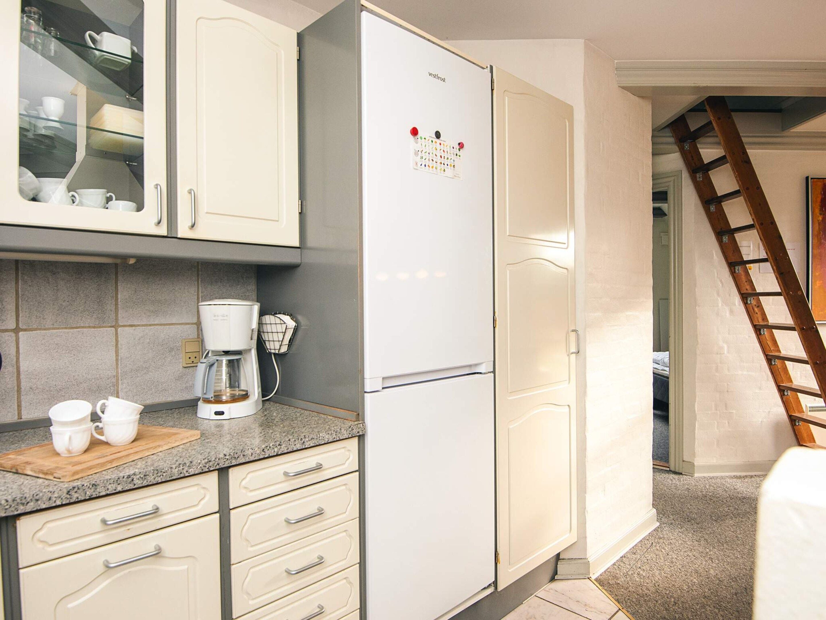 A kitchen with a white refrigerator, a coffee maker, and a countertop with cups.