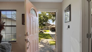 A hallway with a pink door leading to a front yard.